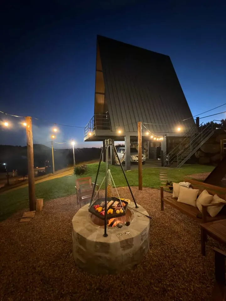Grelha acesa no firepit com a cabana iluminada ao fundo